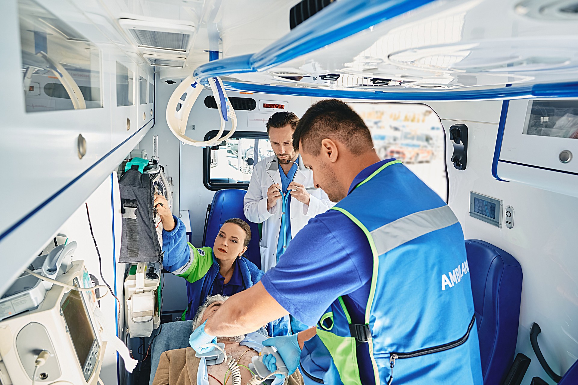 Paramedics with portable defibrillator in attempt to revive male patient inside ambulance, assisted by doctor cardiologist. Victim has heart attack